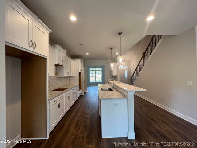 kitchen with sink, dark hardwood / wood-style floors, pendant lighting, a center island with sink, and white cabinets