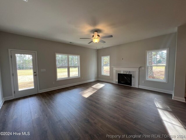 unfurnished living room featuring dark hardwood / wood-style flooring, ceiling fan, plenty of natural light, and a high end fireplace