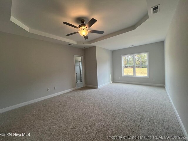 empty room with a tray ceiling, light carpet, and ceiling fan