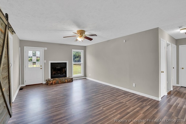 unfurnished living room featuring a textured ceiling, ceiling fan, dark hardwood / wood-style floors, and a barn door