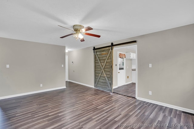 empty room with a barn door, a textured ceiling, dark hardwood / wood-style flooring, and ceiling fan