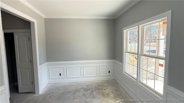 empty room featuring a wainscoted wall, concrete floors, ornamental molding, and a decorative wall