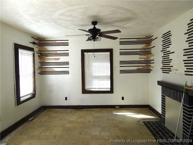 empty room with ceiling fan, a textured ceiling, and a tiled fireplace