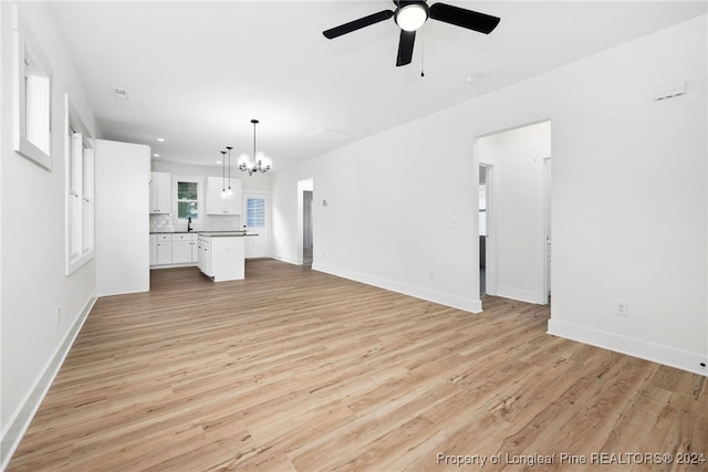 unfurnished living room with ceiling fan with notable chandelier and light hardwood / wood-style floors