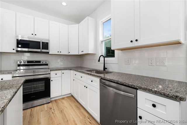 kitchen featuring stainless steel appliances, dark stone counters, sink, light wood-type flooring, and white cabinetry