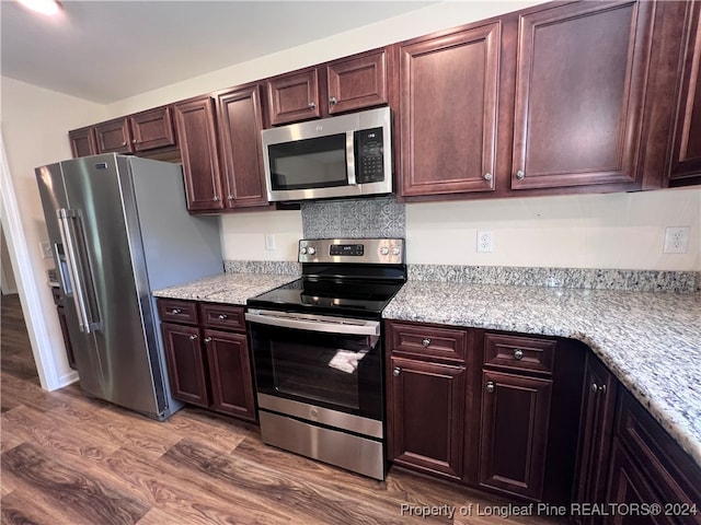 kitchen with appliances with stainless steel finishes, light stone countertops, and dark wood-type flooring