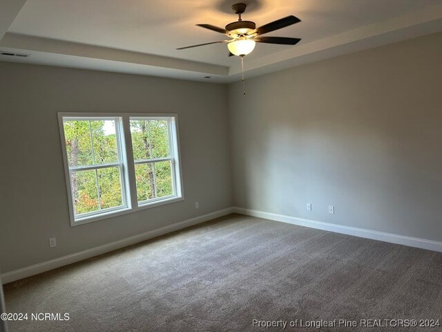 unfurnished room with carpet floors, a tray ceiling, and ceiling fan