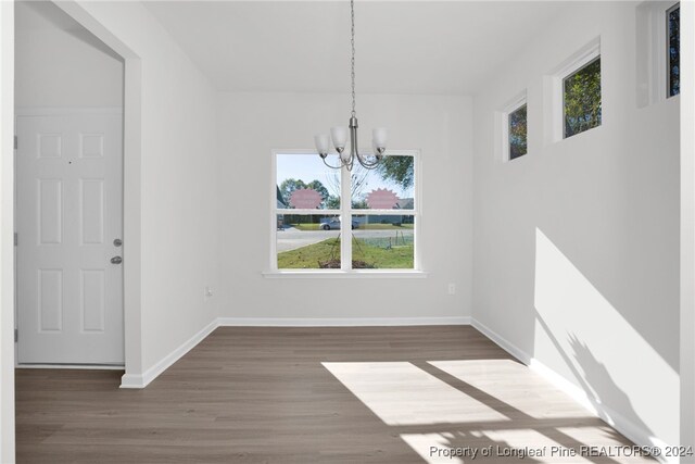 unfurnished dining area featuring dark wood-type flooring and an inviting chandelier