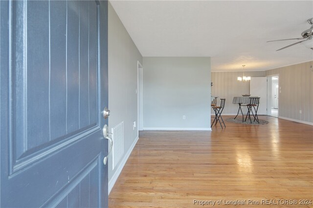 interior space featuring ceiling fan with notable chandelier, wooden walls, and light hardwood / wood-style flooring