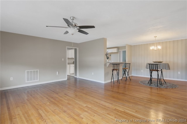 unfurnished living room with ceiling fan with notable chandelier, light wood-type flooring, and wood walls