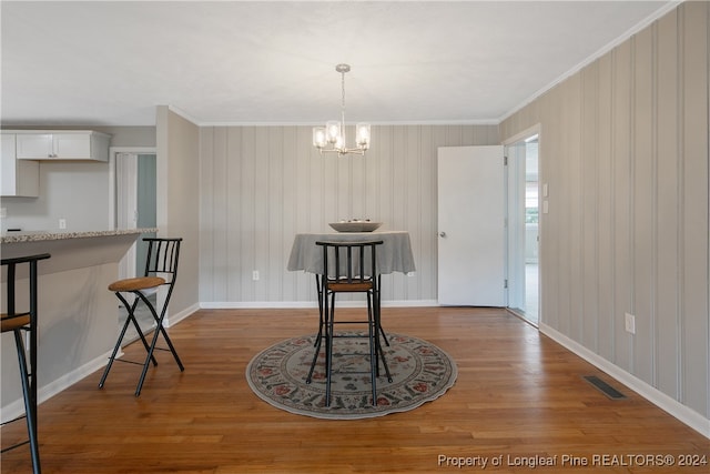 dining area with wood walls, wood-type flooring, ornamental molding, and a chandelier