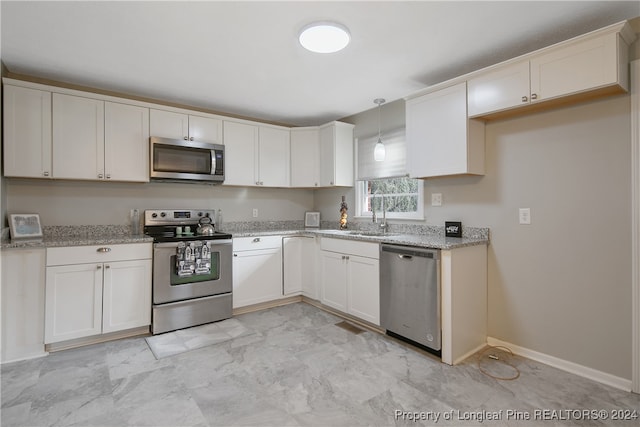 kitchen with appliances with stainless steel finishes, light stone counters, sink, pendant lighting, and white cabinetry