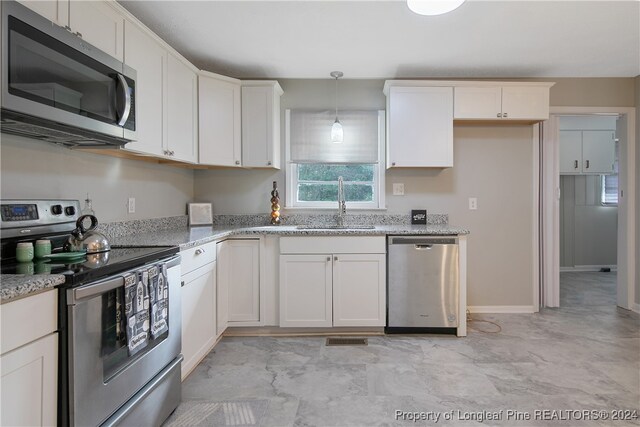 kitchen featuring white cabinetry, light stone countertops, sink, pendant lighting, and appliances with stainless steel finishes