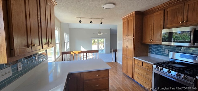 kitchen featuring light wood-type flooring, tasteful backsplash, stainless steel appliances, ceiling fan, and hanging light fixtures