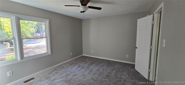 spare room with dark colored carpet, ceiling fan, and a textured ceiling