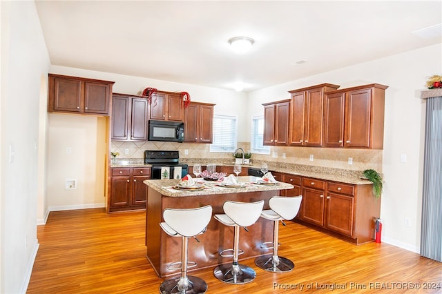 kitchen with backsplash, a breakfast bar, black appliances, light hardwood / wood-style flooring, and a center island