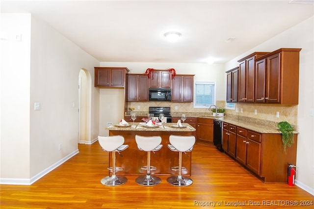 kitchen featuring sink, a kitchen island, black appliances, and light wood-type flooring