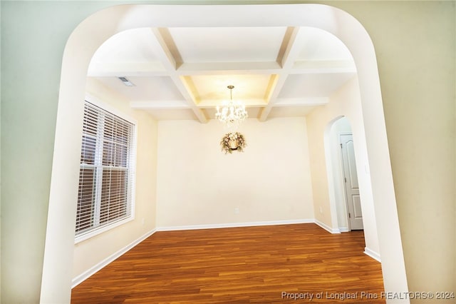 empty room featuring beamed ceiling, a notable chandelier, wood-type flooring, and coffered ceiling