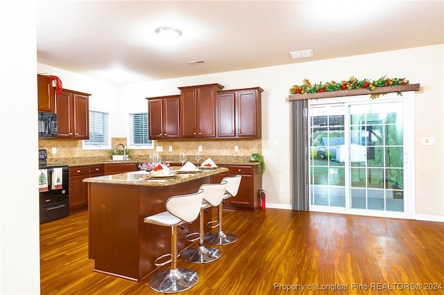 kitchen featuring a healthy amount of sunlight, dark hardwood / wood-style flooring, a kitchen island, and black appliances