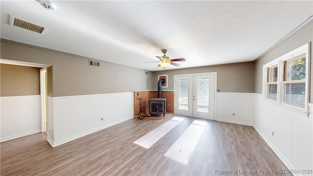 unfurnished living room with a wood stove, ceiling fan, french doors, light hardwood / wood-style flooring, and crown molding