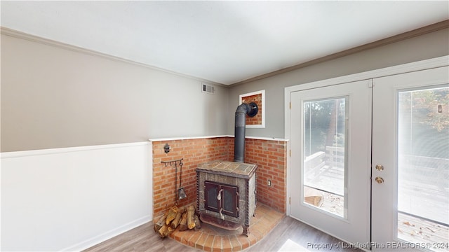 living room featuring french doors, light hardwood / wood-style floors, a wood stove, and ornamental molding