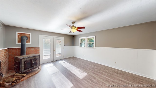 unfurnished living room with a wood stove, ceiling fan, french doors, hardwood / wood-style floors, and ornamental molding