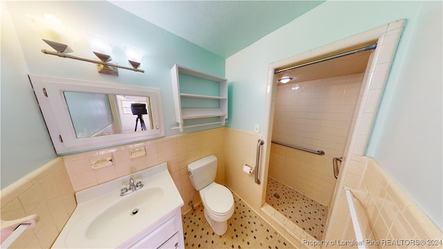 bathroom with vanity, tile patterned floors, toilet, tiled shower, and tile walls