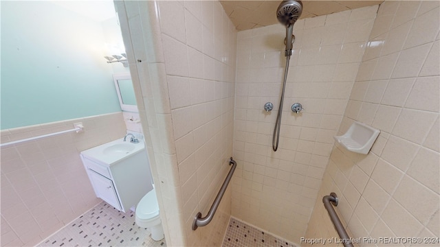 bathroom with a tile shower, vanity, toilet, and tile walls