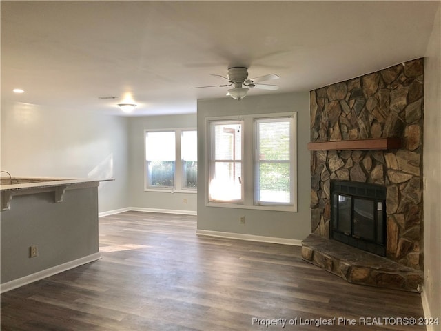 unfurnished living room with a stone fireplace, ceiling fan, and dark hardwood / wood-style flooring