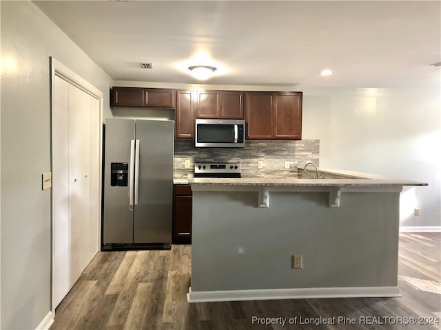 kitchen with a breakfast bar, decorative backsplash, light stone counters, wood-type flooring, and stainless steel appliances