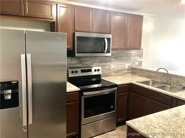 kitchen featuring tasteful backsplash, light stone countertops, sink, and appliances with stainless steel finishes