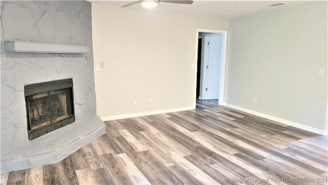 unfurnished living room with wood-type flooring, a textured ceiling, a stone fireplace, and ceiling fan