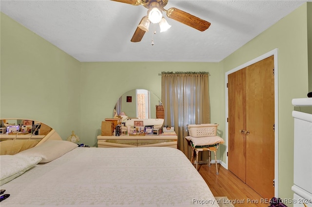 bedroom with ceiling fan, light hardwood / wood-style floors, a textured ceiling, and a closet