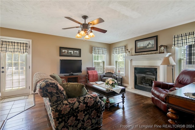 living room featuring ceiling fan, dark hardwood / wood-style flooring, a textured ceiling, and a tiled fireplace