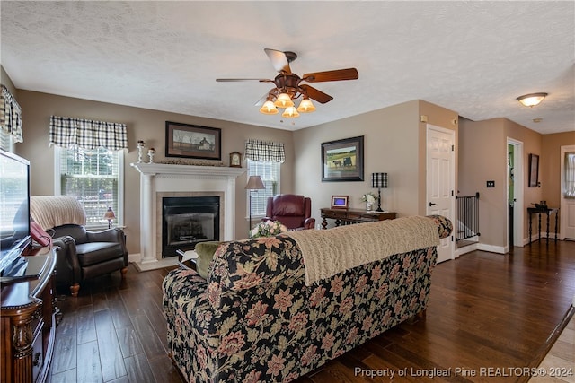 living room featuring a textured ceiling, a tiled fireplace, a healthy amount of sunlight, and dark hardwood / wood-style floors