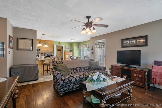 living room with a textured ceiling, ceiling fan, and dark wood-type flooring