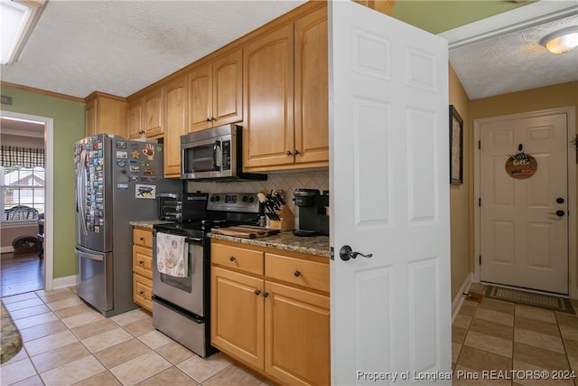 kitchen with dark stone countertops, light tile patterned floors, a textured ceiling, and appliances with stainless steel finishes