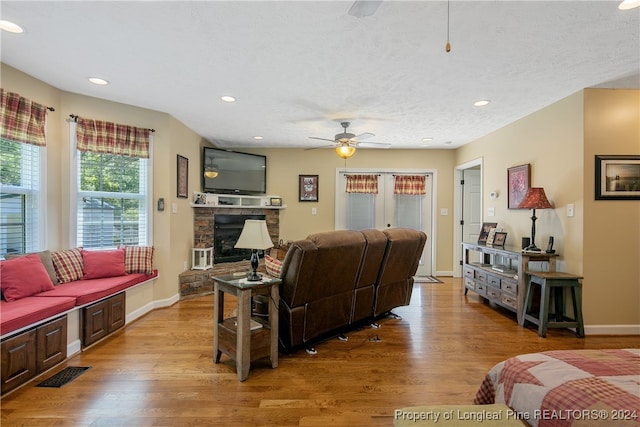 living room featuring ceiling fan, light hardwood / wood-style floors, a fireplace, and french doors