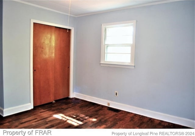 unfurnished bedroom with a closet, dark hardwood / wood-style floors, and ornamental molding