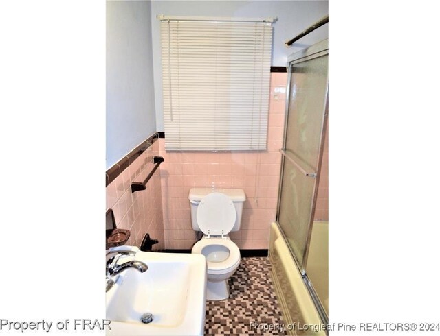 full bathroom with sink, tile patterned flooring, combined bath / shower with glass door, toilet, and tile walls