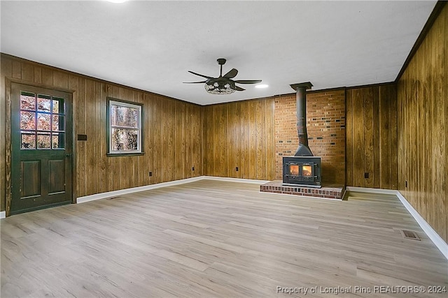 unfurnished living room featuring ceiling fan, a wood stove, wooden walls, and light hardwood / wood-style flooring