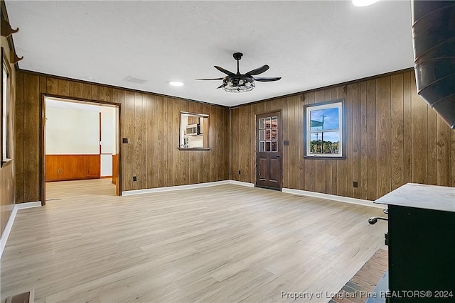 empty room featuring light wood-type flooring, ceiling fan, crown molding, and wood walls