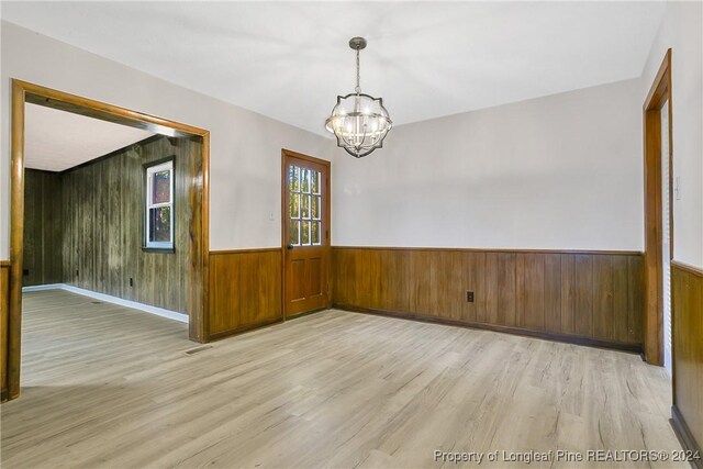 empty room featuring light wood-type flooring, wooden walls, and a notable chandelier