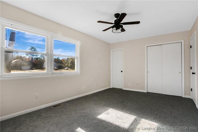 unfurnished bedroom featuring ceiling fan, dark carpet, and a closet