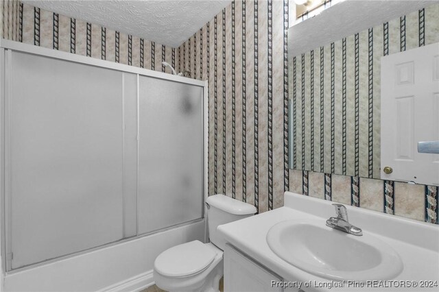 full bathroom featuring vanity, bath / shower combo with glass door, a textured ceiling, and toilet