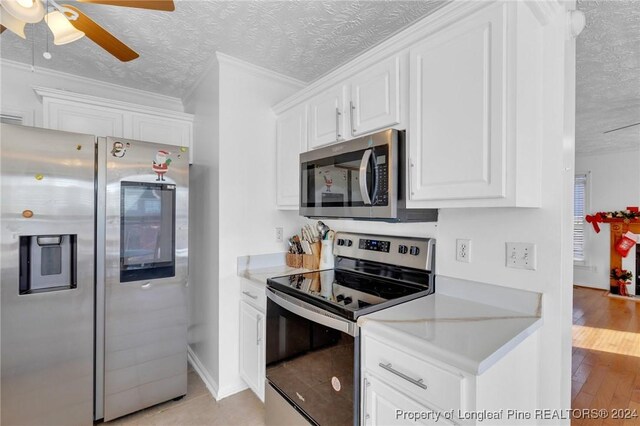 kitchen with white cabinets, crown molding, light wood-type flooring, a textured ceiling, and appliances with stainless steel finishes