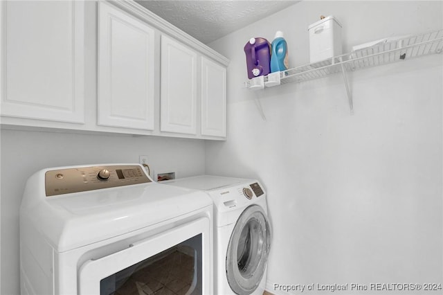 clothes washing area with cabinets, a textured ceiling, and independent washer and dryer