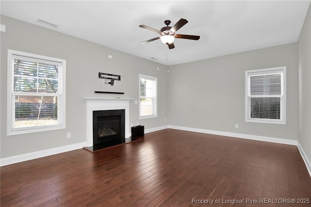 unfurnished living room with ceiling fan, dark wood-type flooring, and a wealth of natural light