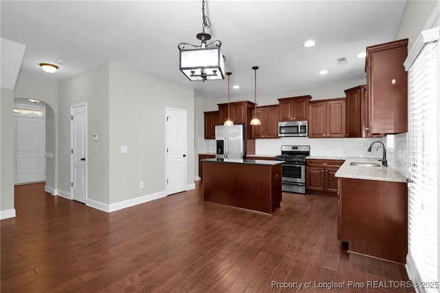 kitchen with sink, dark wood-type flooring, stainless steel appliances, decorative light fixtures, and a kitchen island