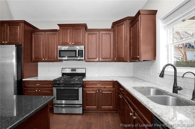 kitchen with backsplash, stainless steel appliances, light stone counters, and sink